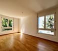 Spacious living room with hardwood floors, large windows overlooking a wooded area, providing a pleasant view of the surrounding nature.