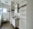 Spacious bathroom with white tiles, a vanity unit with a sink, a toilet, and a towel warmer on the wall.