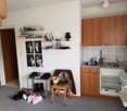 small kitchen with sink, wooden shelves, wooden chair, shoe rack, open refrigerator, photo poster on wall