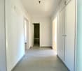 Wide corridor with white walls, gray floor, three doors, one leading to a room