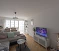 white walls, white shelving, coffee table, grey couch, TV, lamp, windows with curtains