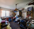 cluttered room with a desk, chair, shelves, and various items