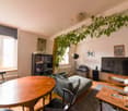 Living room with wooden table, chairs, couch, TV, bookshelf, radiator, window, plant