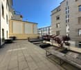 Outdoor area with wooden benches, plants, and a paved floor.