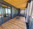 Wooden deck with tables and chairs, balcony with railings, sliding glass doors