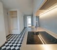 kitchen, black and white checkered tiles, stainless steel countertop, induction hob, sink, faucet, exhaust hood, storage cabinet