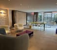 Spacious open-plan living area with comfortable seating, dining table, and large windows providing natural light and access to a balcony or terrace.