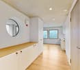 Wooden floor, white walls, circular mirror, white cabinets, two windows