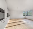 empty room, white walls, wooden floor, large windows, kitchen appliances visible