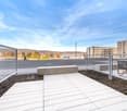 Empty outdoor area with concrete flooring, bench, metal fences, a distant building, and a clear sky.