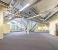 empty interior space with carpeted floor, exposed white ceilings, yellow walls, central stairwell, large windows with view of outside, metal pipes and ducts