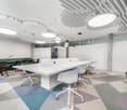 Modern office with a white long desk, various chairs, geometric carpet, round ceiling lights