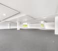 empty room, white walls, gray carpet, recessed lighting, central columns, glass windows with yellow blinds