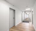Empty hallway with white walls, wooden floor, glass doors, and a black mat at the entrance.