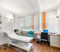 medical examination room with examination table, medical equipment, desk, chair, monitor, cabinets, windows with blinds