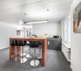 modern kitchen with wooden counter, black bar stools, white walls, gray cabinets, white radiator, microwave, sink, picture frame