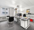 modern office with white walls, gray carpet, white desks, black chairs, computer monitors, radiator, cabinets, and a window with a view