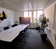 A conference room with a long table, black chairs, a whiteboard, a TV, and a potted plant.