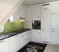 Modern kitchen with white cabinets, stainless steel sink, integrated oven, green splashback, tiled floor