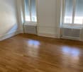 empty room with white walls, wooden floor, two windows, and white radiators