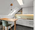 small kitchen with wooden table, white cabinets, green chairs, skylight, pendant light, sink, countertop, refrigerator