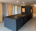 modern kitchen with central island, black countertops, silver handles, wooden cabinets, wooden floor, ceiling lights
