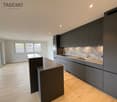 modern kitchen, wooden floor, black island, black cabinets, silver sink, stainless steel faucet, white walls, large windows, empty room