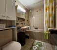 Bathroom with toilet, sink, bathtub, storage shelves, mirror and shower curtain.