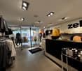 A clothing store with multiple sections for different clothing, large clothing racks, and a black rug with Zeb written on it.