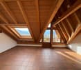 Empty attic room with wooden beams, tiled floor, windows, and scenic view