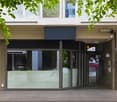 Corner building with glass doors and windows, open entrance with revolving door, two shops with glass windows and doors.