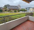Balcony with metal railing, red brick floor, view of a grassy field and houses