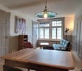 A room with a wooden table, a couch, a chair, a shelf, a lamp, a painting, and a window.
