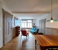 Empty room with wooden floor, white walls, wooden table, red chair, blue couch, wooden cabinet, window, lamp