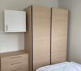 bedroom, a cabinet, drawers, wardrobe with sliding doors, bed with white blanket and pillow