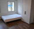White bed, white wardrobe, white walls, windows with outdoor view, wooden floor.