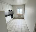The image shows a kitchen with white cabinets, a tiled floor, and a window overlooking the exterior. The kitchen appears to have a stove, oven, and other appliances.