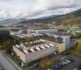 Industrial area with various buildings, large parking area, mountains in the background