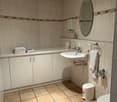 white tiled wall, white tiled floor, white cabinet, sink, mirror, faucet, towel rack, toilet, wastebasket