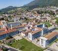 This image shows an aerial view of a city nestled in a mountainous landscape. The city has a mix of modern and traditional architecture, with a combination of high-rise buildings, residential homes, and historic structures. The city is surrounded by lush