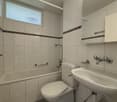 Bathroom with white tiles, bathtub, toilet, sink, mirror, and shower head