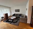Living room with wooden floor, two sofas, coffee table, rug, wooden cabinet, lamp, picture frame, and white curtains
