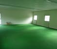 Empty room, fluorescent ceiling lights, green flooring, three windows, storage box on the floor.
