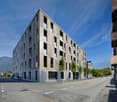 Modern apartment building with multiple floors, concrete and glass exterior, multiple windows, and a flat roof.