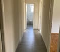 Empty hallway with tiled floor, white walls, and wooden floor in the right corner.