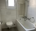 Bathroom with white tiles, bathtub, toilet, sink, window, radiator, shower head, and towel rack.
