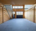 Large open space with concrete floor, wooden walls, and a metal staircase. The space appears to be a garage or workshop area with a garage door visible at the back.