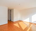 Empty room with hardwood floors, white walls, sunlight through the windows, power outlets on the walls