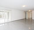 Large, empty room with white walls, ceiling, tiled floor, sliding glass doors leading to balcony, white ceiling lights