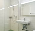 modern bathroom with white tiles, glass shower enclosure, white sink, chrome fixtures, green floor tiles